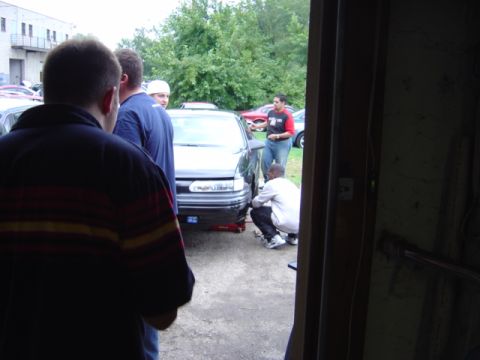 1998 Ford Taurus - Several people observe a car being worked on in an outdoor setting.