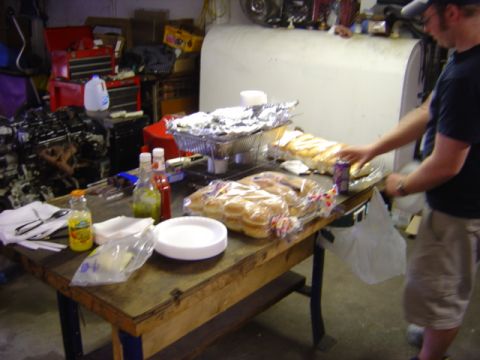 1998 Ford Taurus - An engine block sits on a table laden with food, including buns and foil-wrapped dishes.