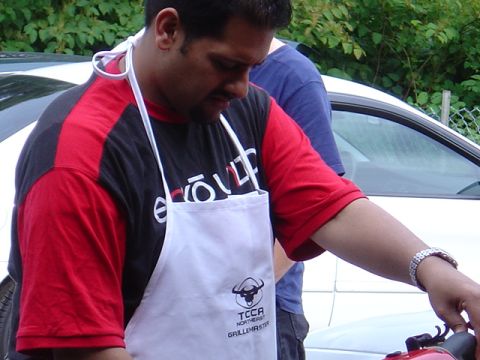 1998 Ford Taurus - Man wearing a TCCA Northeast Grillemaster apron stands near a white car.