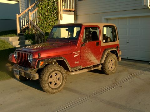 1998 Jeep TJ - A red Jeep Wrangler with a tan top is parked in a driveway, showing mud splashes on its side.