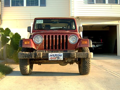 1998 Jeep TJ - A red 1998 Jeep TJ is parked in front of a garage, showing its front grille and license plate.