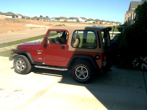 1998 Jeep TJ - Side view of a red 1998 Jeep TJ Wrangler with a tan soft top parked on a concrete driveway.