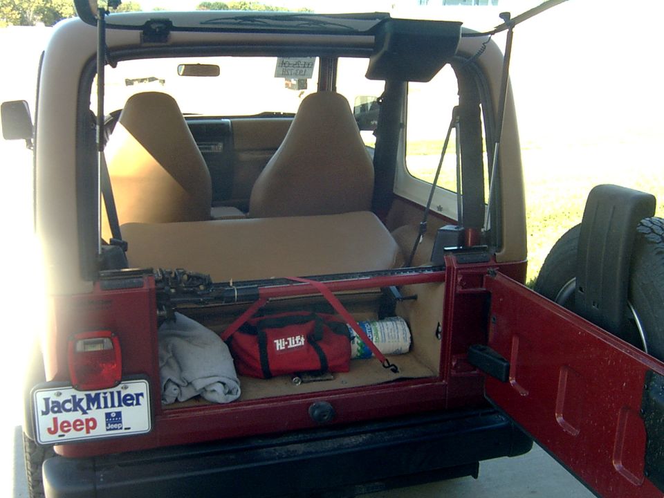Open tailgate of a red Jeep Wrangler with Hi-Lift bag, jack and rope strapped in cargo area