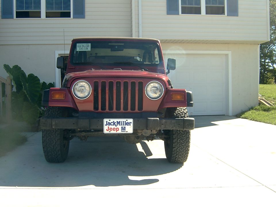 Front view of red Jeep Wrangler TJ with tan soft top parked in front of a house