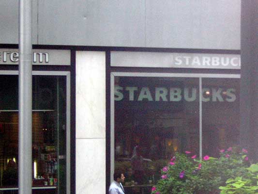 Starbucks storefront with large windows reflecting the interior and a man standing outside