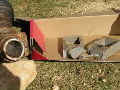 1989 Ford Bronco - Driveshaft U-joint and broken metal pieces are laid out on the grass.