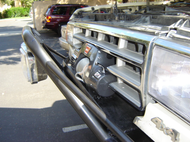 Black winch mounted on tubular bull bar of a light-colored 4x4 truck front end.