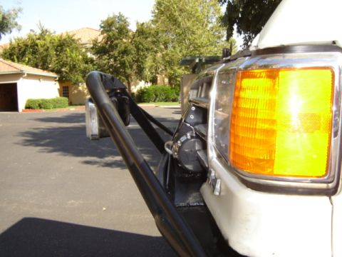 1991 Ford Bronco - Close-up of the front corner of a white 1991 Ford Bronco, showing the turn signal, grille, and a bull bar.