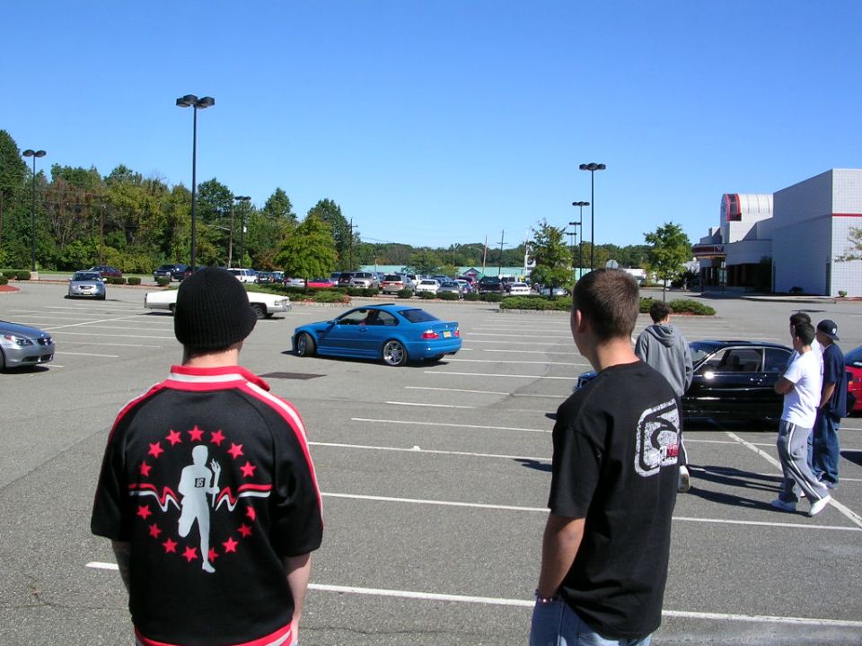 Blue BMW E46 M3 coupe rolling through a parking-lot car meet as spectators watch