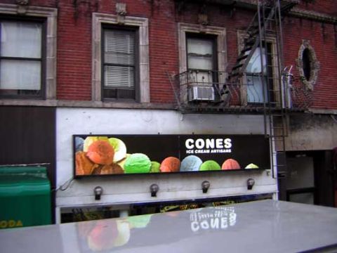 1995 Ford Bronco - A storefront displays a large advertisement for CONES ICE CREAM ARTISANS, colorful scoops of ice cream.