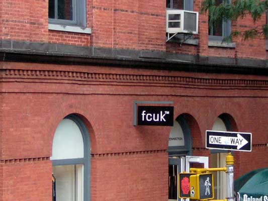 Brick building with arched windows and a "fcuk" sign. A "ONE WAY" sign and traffic signals are visible