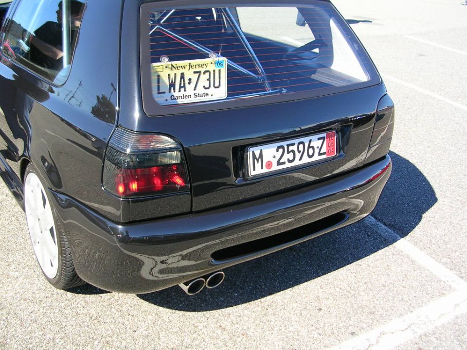 Black Volkswagen hatchback rear view, showing dual exhaust pipes and New Jersey license plate LWA-73U