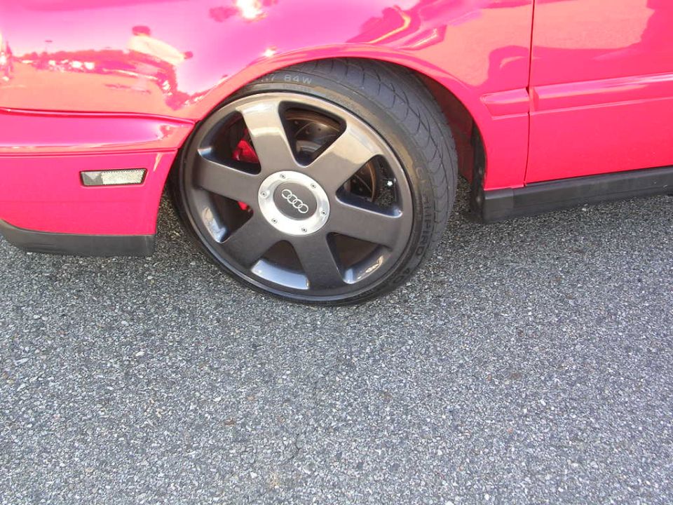 Close-up of a pink car's fender and a dark gray Audi wheel with red brake calipers visible