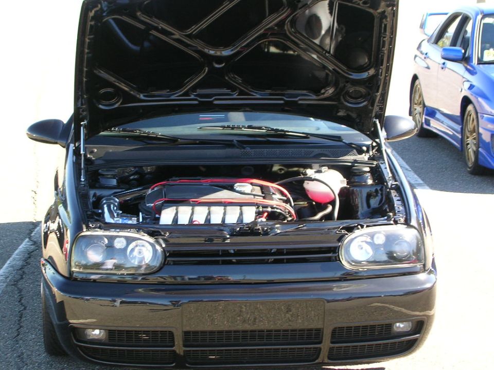 Black Volkswagen Golf Mk3 with hood open, showing engine. Headlights are aftermarket. Another blue car is visible to the right