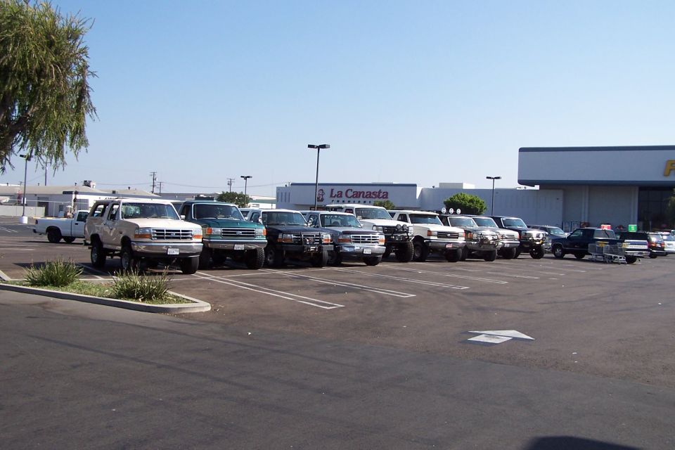 Several trucks and SUVs parked in a lot, including a white Ford Bronco from the mid-1990s