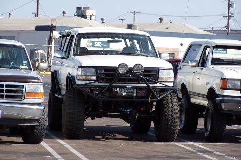 1990 Ford Bronco - A modified 1990 Ford Bronco is parked in a lot, flanked by other vehicles.