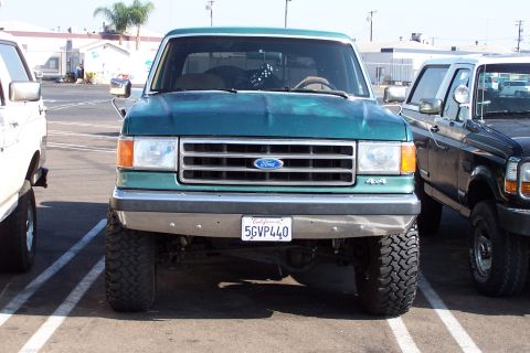 1990 Ford Bronco - This green Ford truck, possibly a 1990 model, is parked next to another truck.