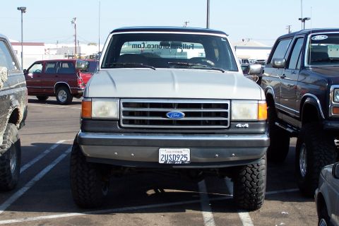 1990 Ford Bronco - This lifted Ford Bronco is parked in a lot with other vehicles. The grille and headlights suggest it is from the late 1980s.