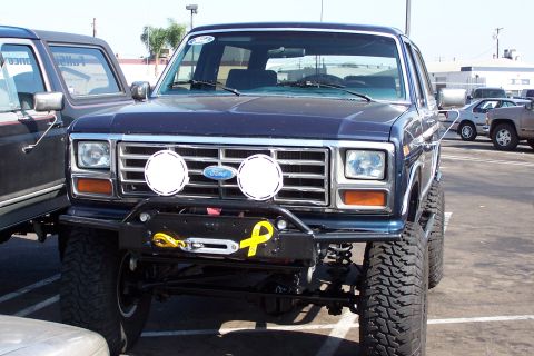 1990 Ford Bronco - A lifted dark blue Ford Bronco with a winch and auxiliary lights is parked in a lot.