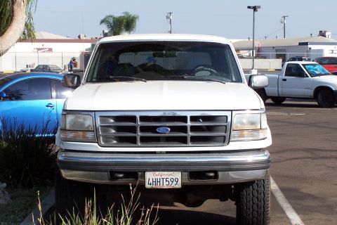 1990 Ford Bronco - Front view of a white Ford Bronco parked in a lot with another truck visible.