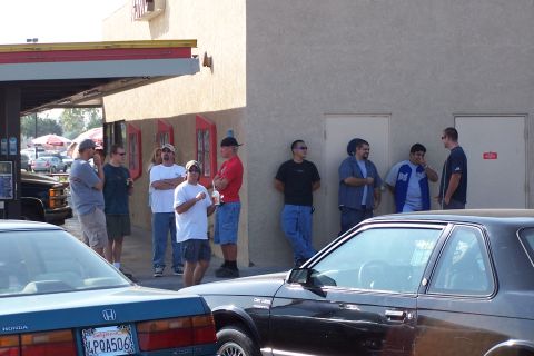 1990 Ford Bronco - A group of men gather outside a building on a sunny day, with several vehicles visible.