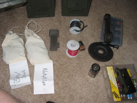 1988 Ford Bronco - Various hardware items, including wire, batteries, and fasteners, are laid out on a carpeted floor next to two green storage containers.