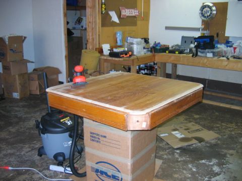 1985 Ford LTD Crown Victoria - A wooden tabletop is being sanded in a garage setting, with tools and boxes visible in the background.