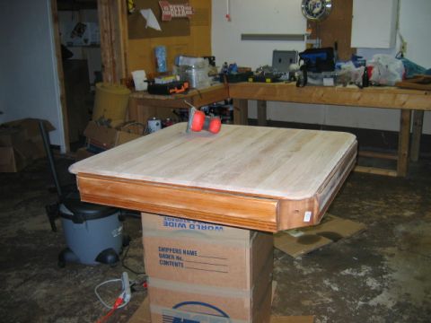 1985 Ford LTD Crown Victoria - A wooden tabletop is elevated on cardboard boxes in a workshop setting, with tools and supplies visible on shelves.