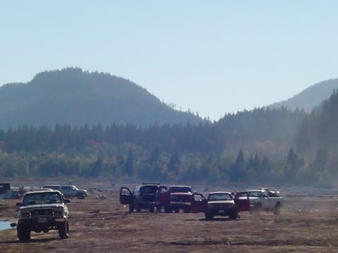 1993 Ford Bronco - Several SUVs and trucks are parked in a dry, open area with hills and trees in the background.