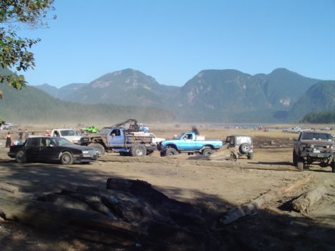 1993 Ford Bronco - A collection of trucks and a sedan are gathered on a dirt lot, with mountains visible in the distance.