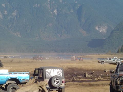 1993 Ford Bronco - A black Jeep Wrangler is parked in a muddy field with mountains in the background.