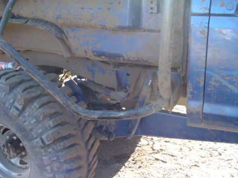 1993 Ford Bronco - Side view of a heavily modified blue off-road vehicle with large tires and a roll cage, covered in mud.