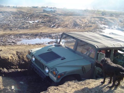 1993 Ford Bronco - A military vehicle is stuck in a muddy ditch while other vehicles are visible in the background.