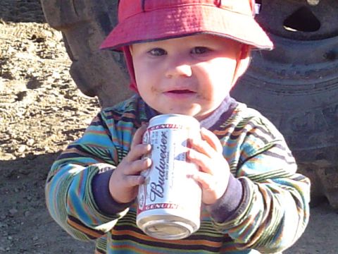 1993 Ford Bronco - A young child, wearing a red hat and a striped shirt, holds a can of Budweiser in front of a large tire.