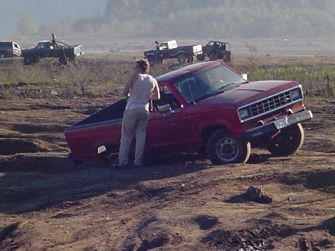 1993 Ford Bronco - A red pickup truck is stuck in the mud while other vehicles are visible in the background.