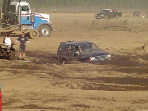 1993 Ford Bronco - A black SUV is stuck in a muddy area, with a large truck and an ATV visible in the background.