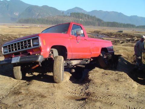 1993 Ford Bronco - Red pickup truck navigating a challenging off-road terrain with mountains in the background.