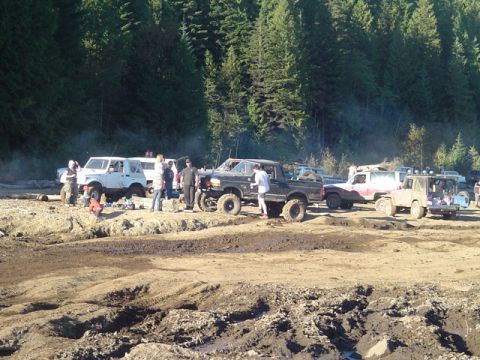 1993 Ford Bronco - Several off-road vehicles are gathered on a muddy track with a forest backdrop.