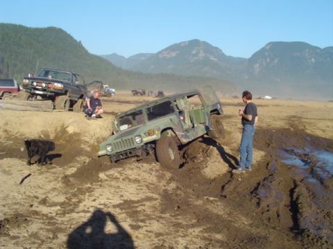 1993 Ford Bronco - Off-road vehicles navigate a muddy terrain with mountains in the distance.