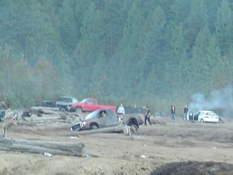1993 Ford Bronco - Several vehicles are in a muddy area with people standing around and smoke rising from one car.