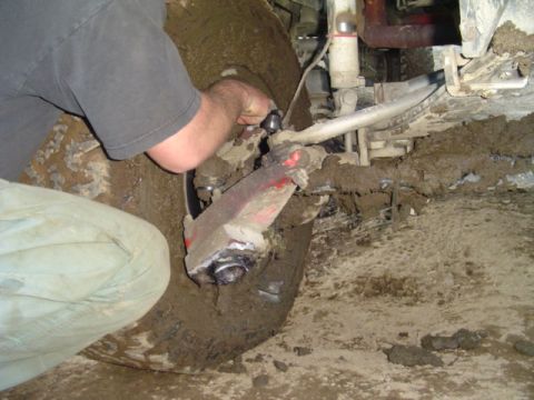 1993 Ford Bronco - Mechanic works on the muddy front suspension and tire of a 1993 Ford Bronco.