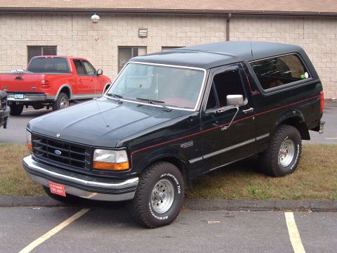 1993 Ford Bronco - A black 1993 Ford Bronco with red pinstriping is parked next to a red pickup truck.