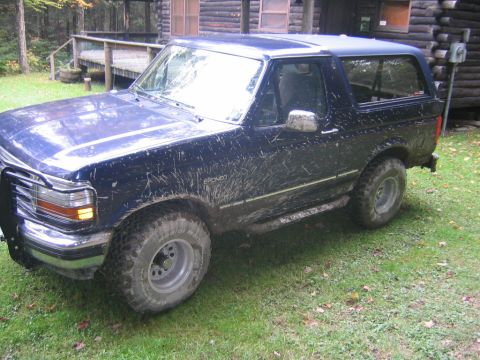 1994 Ford Bronco - A muddy Ford Bronco sits on a grassy lawn next to a wooden cabin.