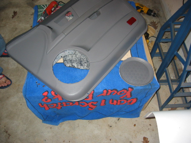 Gray Taurus door panel with speaker grille removed, resting on a blue towel in a garage