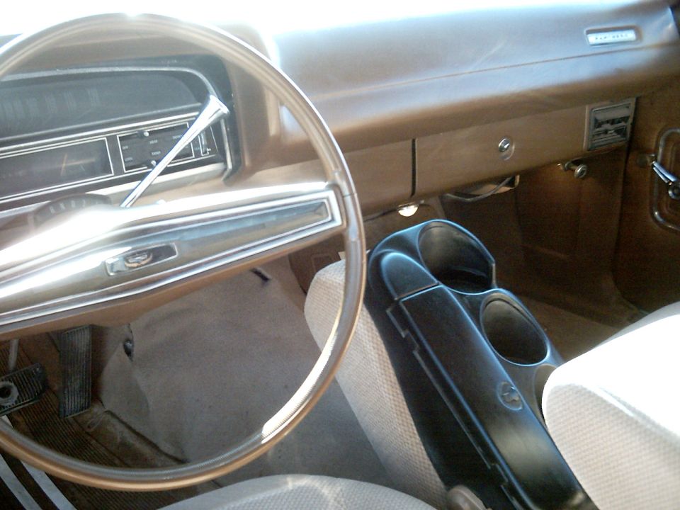 Interior of a classic Ford with brown dash, large steering wheel, tan seats, and black center console cup holders