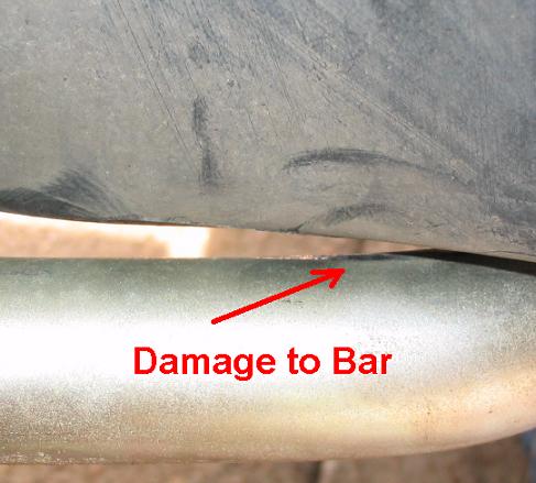 Close-up of damage to a metal bar, with red arrow and text