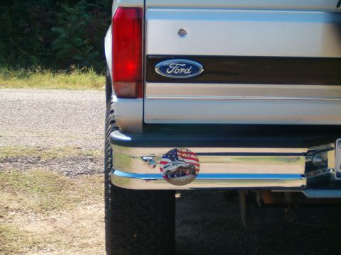 1996 Ford Bronco - The rear of a vehicle shows a Ford emblem and a sticker with trucks on it.