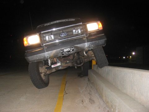 1988 Ford Bronco - This Ford Bronco is precariously balanced on a concrete barrier, with its front wheels elevated.