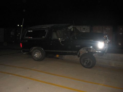 1988 Ford Bronco - A black Ford Bronco is parked outdoors at night, illuminated by its headlights.