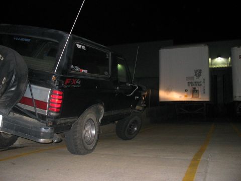 1988 Ford Bronco - This Ford Bronco has a flat tire and is parked near a semi-trailer at night.